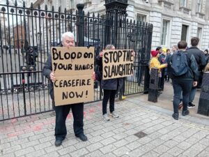 Chris Cole and Virginia Moffat hold protest placards calling for a Gaza ceasefire and end to UK complicity in the slaughter. 
